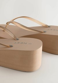 Tongs à plateforme beige avec brides translucides et semelles texturées, arborant la marque "NEXT" et une semelle compensée.