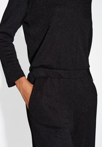 Top in tessuto nero effetto testurizzato caratterizzato da una vestibilità aderente con maniche lunghe, completato da una vita abbinata e da sottili dettagli metallici.