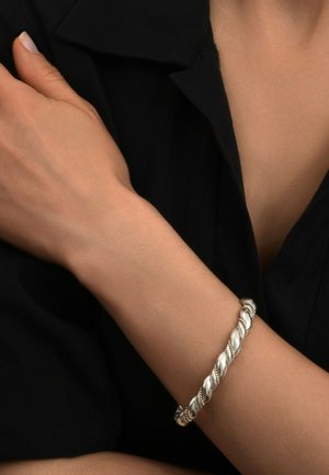 Bracelet en argent torsadé avec des détails élaborés, s'ajustant parfaitement autour d'un poignet, présenté sur un fond sombre. Surface lisse et réfléchissante.