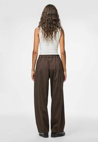 Rudos dryžuotos plataus kojų silueto kelnės su elastine juosmens juosta, pasižyminčios lygiu paviršiumi ir laisvu kirpimu. Matomas paprastas baltas berankovis marškinėlis.