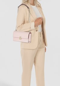 Light pink leather handbag with a fold-over flap, gold hardware, and a chain strap, showcased against a neutral background.