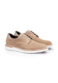 Scarpe beige in suede stringate con punta arrotondata, suola bianca a contrasto e dettagli di cucitura discreti lungo i pannelli laterali.