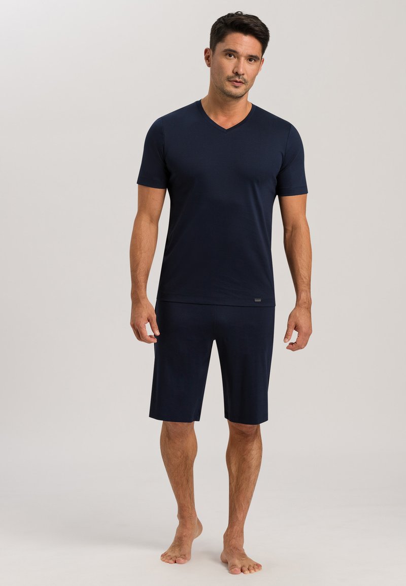 Navyblaues kurzärmliges V-Ausschnitt-Oberteil, kombiniert mit knielangen Shorts. Hergestellt aus einem weichen Stoff mit glatter Textur und einem taillierten Schnitt.