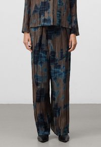 Twee-delige outfit in geplooide stof met een bruine basis en blauwe abstracte patronen. Losvallend, gecombineerd met zwarte schoenen.