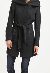 Black coat with a hood, belted waist, and two zippered pockets. Features a textured fabric and a streamlined silhouette.