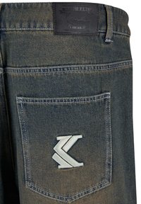 Denim jeans with a faded blue color, featuring a leather patch and an embroidered stylized logo on the back pocket. Classic five-pocket design.