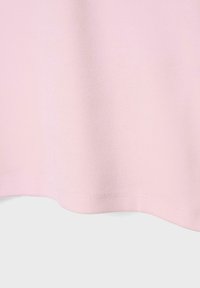 Tissu rose clair avec une fine texture côtelée montré en gros plan, mettant l'accent sur le bord inférieur et la couture de l'ourlet.