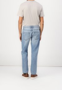 Světle modré džíny z denimu s rovnými nohavicemi, mají dvě zadní kapsy a kontrastní švy; nošeny s krátkým šedým tričkem a hnědými botami.