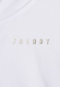 Camiseta de algodón blanca con la palabra "FREDDY" bordada en hilo metálico dorado, con un cuello redondo y textura acanalada.