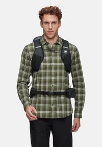Zwarte en grijze hydratatiepack gedragen over een groen geruite shirt. Voorzien van verstelbare banden, vakken en een gesp in de taille.
