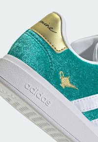 Mokasíny z modré suede s bílými pruhy, zlaceným poutkem na patě a vyšívaným detailem. Mají texturovanou podrážku a značkovou stranu.