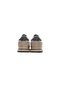 Zapatillas que combinan cuero beige y ante gris, con un acento azul marino oscuro en el talón y una suela de goma beige con rayas.