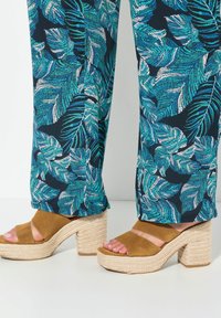 Pantalon large avec un motif de feuilles tropicales bleues et des sandales à plateforme en daim marron avec des détails en corde et des sangles larges.