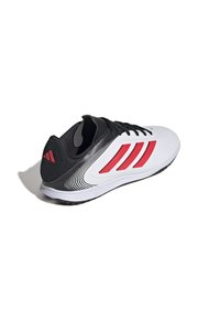 Zapatilla deportiva en blanco y negro con acentos rojos, material sintético suave, diseño de cordones y suela texturizada para mayor agarre.