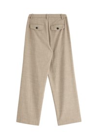 Beige vida byxor i texturerat tyg, med två bakfickor med svarta knappar och en slät framsida.