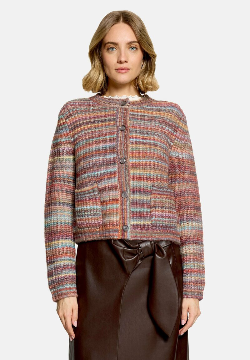 Femme portant un cardigan en tricot rayé multicolore par-dessus un haut blanc et une jupe en cuir marron foncé avec un détail noué à la taille.