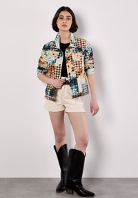 Chaqueta de mezclilla con estampado de pata de gallo colorido, de mangas largas, camiseta negra, pantalones cortos crema y botas de estilo vaquero negras. Textura suave.