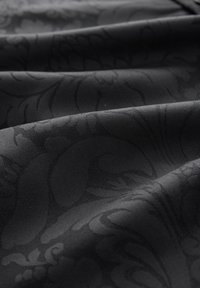 Tessuto nero con un delicato motivo floreale, caratterizzato da una texture liscia e pieghe strutturate, che mostrano profondità e dimensione.