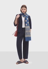 Mornarska teksturirana jakna, bijela majica i mornarske hlače. Plavi šal s laganim uzorcima. Prugaste sandale s otvorenim prstima. Crvena torba. Ležerna odjeća.