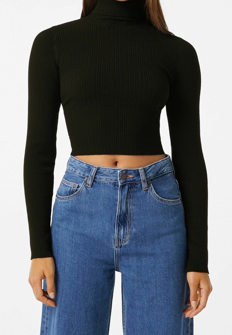 Svart ribbad polokrage kort topp i kombination med högmidjade ljusblå jeans. Toppens ärmar är långa och designen är åtsittande.