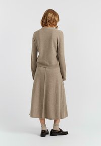 Maglione beige lavorato a maglia e gonna lunga abbinata, entrambi realizzati in tessuto morbido. Il vestito presenta una silhouette svasata e dettagli di cucitura sottili.