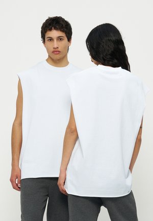 Kaks moodelit kannavad varrukatuid valgeid toppe ja tumedaid halli pükse, üks on näoga ettepoole ja teine pööratuna tagasi, ühtlasel heledal taustal.