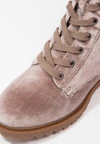 Bottines en velours rose pâle avec des lacets marron clair et des œillets en métal, présentant une surface texturée et une semelle en caoutchouc.