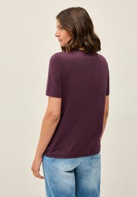 Camiseta de manga corta, cuello redondo, color púrpura, mostrada desde la parte de atrás, combinada con jeans de color azul claro, con una textura suave.
