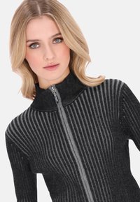 Fekete és szürke bordázott pulóver magas gallérral, cipzáras záródással, és függőlegesen futó, texturált csíkokkal a szöveten.