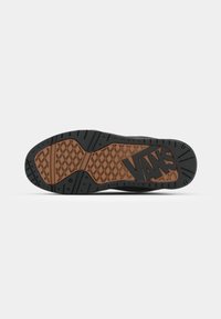 Vans sneaker zool met een zwarte rubberen buitenzijde en bruine textuuraccenten. Beschikt over een hexagonaal patroon en een zichtbaar merklogo.