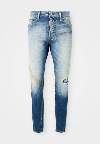Jeans skinny sbiaditi blu chiaro con un piccolo strappo sulla coscia destra e un'etichetta rossa del marchio vicino alla cerniera anteriore.