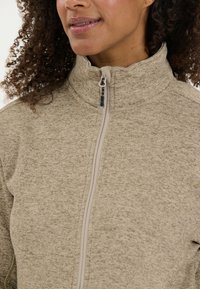 Fleecejacka i beige med hög krage och dragkedjedetalj. Texturerad tyg med ett subtilt mönster. Utformad för värme och komfort.