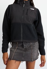 Svart fleecetröja med hög krage, dragkedja och framfickor, kombinerad med en sliten svart jeanskjol.