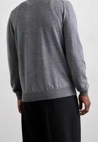 Pull gris en tricot avec un col rond, des poignets et un ourlet côtelés. Le tissu semble doux avec une texture lisse. Pantalon noir visible en dessous.