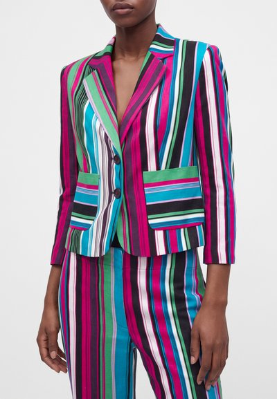 Femme portant un blazer à rayures verticales colorées et un pantalon assorti rose, vert, bleu, noir et blanc avec deux poches devant et des boutons.
