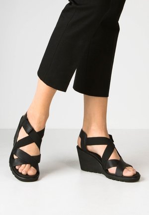 Black wedge sandals with crisscross straps, made of smooth synthetic material. Features a textured sole and open toe design.