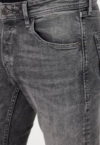 Grijze denim jeans met een zachte textuur, voorzien van een klassiek vijf-pocketontwerp, metalen hardware en subtiele vervagingdetails op de stof.