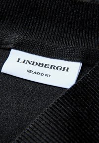 Czarny dziany sweter z prążkowanym kołnierzem, z białą metką z napisem "LINDBERGH RELAXED FIT", ukazujący teksturowaną tkaninę.