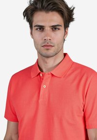 Koralle Polohemd mit klassischem Kragen, zwei Knöpfen und kurzen Ärmeln. Hergestellt aus strukturiertem Baumwollstoff.