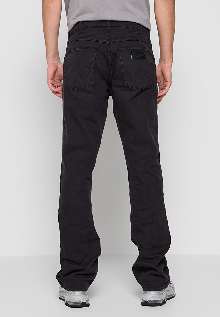 Schwarze Baumwollhosen mit geradem Bein, zwei Gesäßtaschen und einem Markenschild über der rechten Tasche. Getragen mit einem grauen T-Shirt und Schuhen.