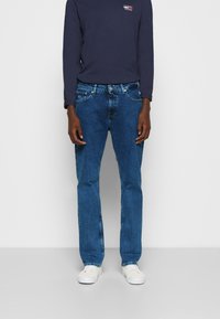 Blå denimjeans med rak passform, som har en klassisk femfickdesign och ljusa blekningar. Bärs med en långärmad marinblå skjorta.