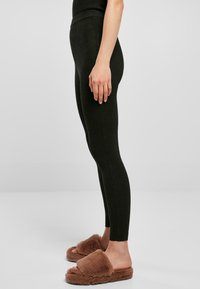 Svart, rillede tights med høj talje, parret med brune, fuzzy slidesandaler. Tightsene har en tætsiddende pasform og en glat tekstur.