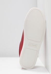 Baskets rouges avec une tige texturée, semelle en caoutchouc blanche et motif à rayures horizontales. Comprend un logo sur la semelle et un design incurvé.