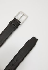 Cinturón de cuero negro con una hebilla rectangular de metal plateado, que presenta una textura suave y múltiples perforaciones para un ajuste ajustable.
