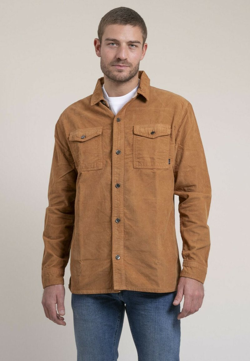 Chemise en velours côtelé marron avec deux poches poitrine, fermeture à boutons à l'avant et coupe droite. Texture douce avec un col classique.