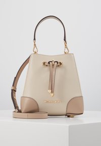 Sac seau en cuir beige avec un design structuré, des ferrures dorées, un système de fermeture à cordon et une bandoulière amovible. Présente un logo.