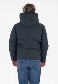 Ciemnoszara kurtka puchowa z kapturem, cechująca się gładką teksturą i minimalistycznym designem. W połączeniu z niebieskimi dżinsami, widoczny szew z tyłu.