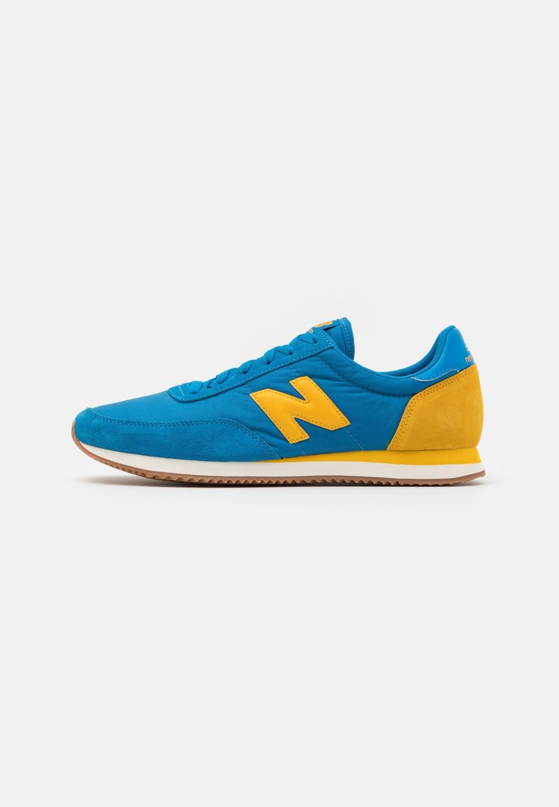 Chaussure de sport bleue et jaune en matériau en suède et textile, avec un logo "N" jaune bien visible, semelle en caoutchouc et talon rembourré.