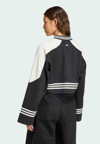 Sweatshirt en noir et crème avec des blocs de couleurs, manches longues, accents rayés près de l'ourlet et un logo au dos de l'encolure.