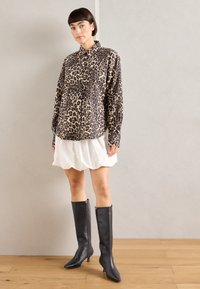 Camicia a stampa leopardata in morbido tessuto, con bottoni e colletto, abbinata a una gonna bianca e stivali alti fino al ginocchio in pelle nera.